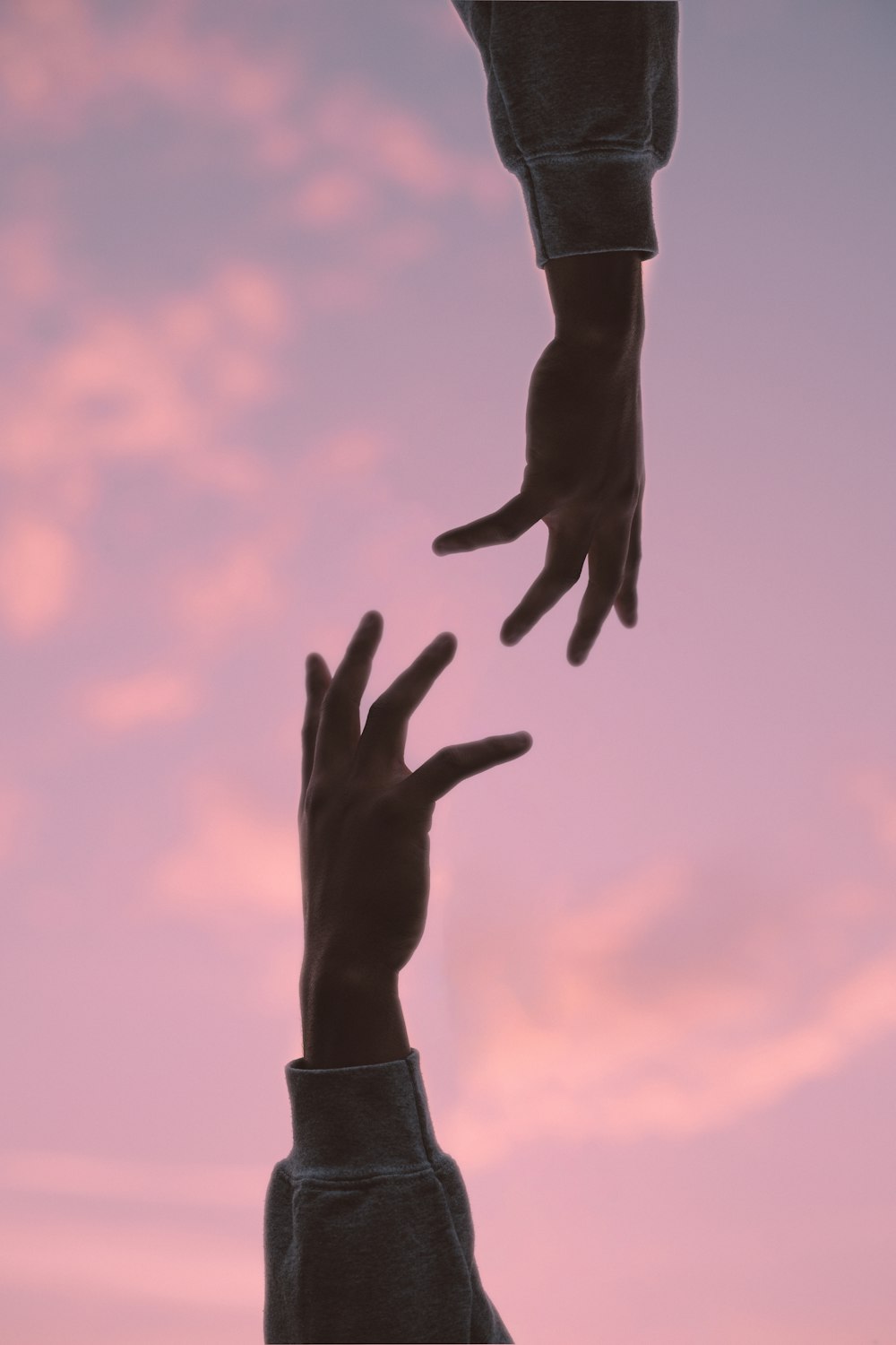 two hands reaching towards each other in front of a pink sky