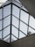 A geometric, triangular glass roof structure with clear panels, supported by a metal framework. Two figures are visible standing on the structure, partially obscured by the glass, interacting with the roof. The background shows a pale blue sky.