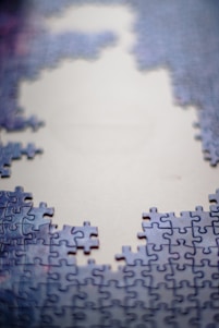 Partially assembled jigsaw puzzle with blue and purple pieces surrounding a large, unfilled area in the center, suggesting an incomplete image.