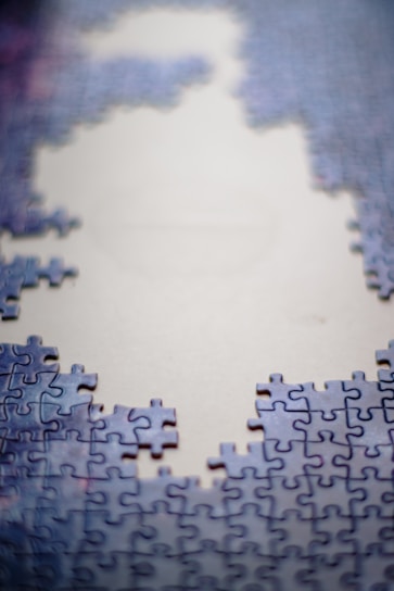 Partially assembled jigsaw puzzle with blue and purple pieces surrounding a large, unfilled area in the center, suggesting an incomplete image.