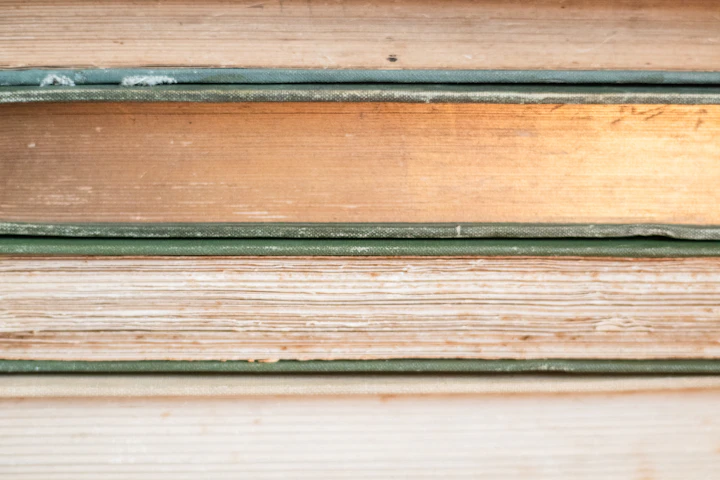 A close stack of weathered antique book spines in warm, muted tones