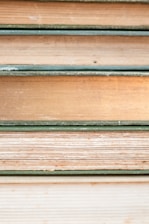 Several stacked books showing their aged and textured spines and pages, varying in color from shades of cream to light brown. Each book is bound with a greenish cover, hinting at their vintage nature.