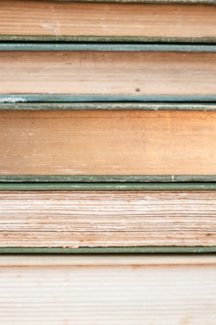Several stacked books showing their aged and textured spines and pages, varying in color from shades of cream to light brown. Each book is bound with a greenish cover, hinting at their vintage nature.