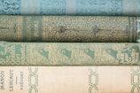 Stack of elegantly bound novels with a subtle pastel background and a pen resting on top.