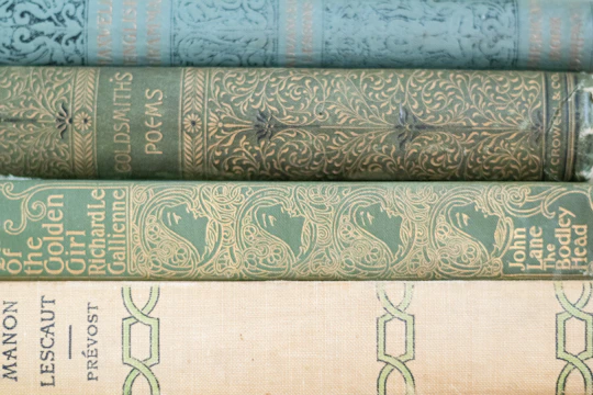 A stack of vintage hardcover books with delicate gold embossing on a beige linen cloth.