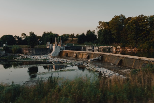 An engineer reviewing water treatment plant blueprints beside a calm reservoir at sunrise.