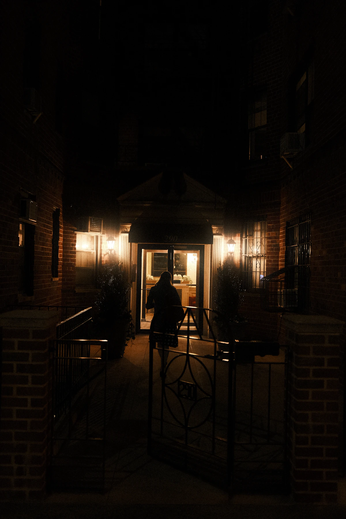 A person stands by a warmly lit doorway on a dark New York street