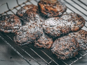 A batch of freshly baked cookies dusted with powdered sugar rests on a cooling rack. The cookies have a rich, dark color indicating they are likely chocolate-based.