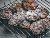 A batch of freshly baked cookies dusted with powdered sugar rests on a cooling rack. The cookies have a rich, dark color indicating they are likely chocolate-based.