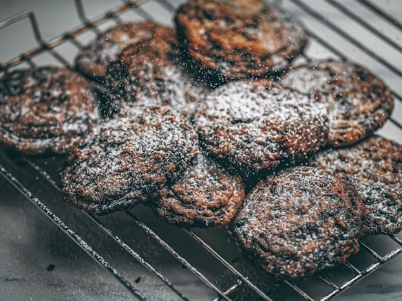 A batch of freshly baked cookies dusted with powdered sugar rests on a cooling rack. The cookies have a rich, dark color indicating they are likely chocolate-based.
