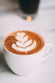 Close-up of a steaming cappuccino with delicate latte art in a cream-colored cup on a soft brown table.