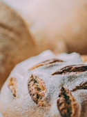 Close-up of freshly baked artisan bread with a golden-brown crust and a dusting of flour. The bread features deep cuts or slashes on the surface, highlighting its rustic texture.