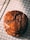A stack of rich, chocolate cookies with a cracked surface, resting on a cooling rack. The texture appears chewy and moist, suggesting freshly baked goodness. Light shines on the cookies, highlighting their glossy and slightly uneven surface.