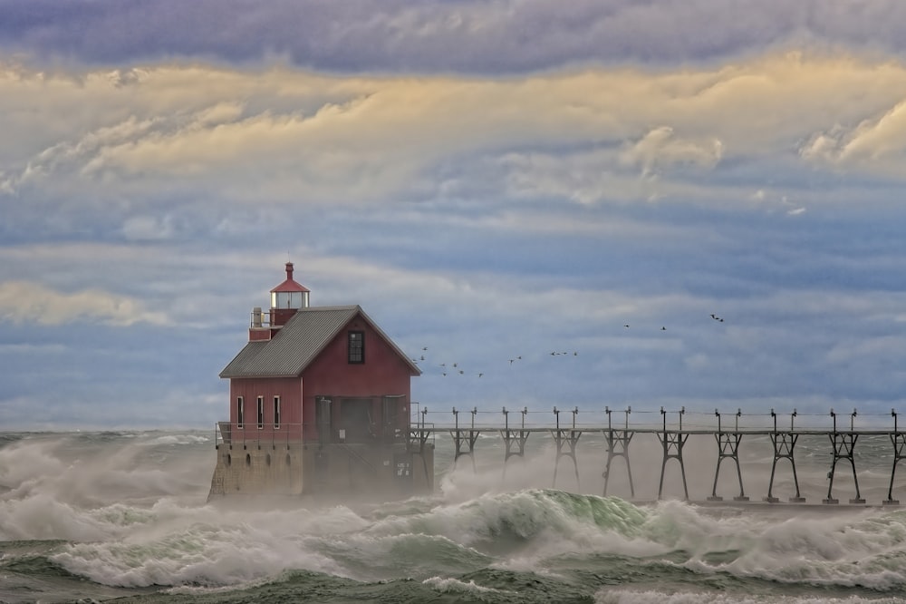 a red house sitting on top of a pier next to the ocean