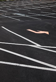 An empty parking lot with neatly painted white lines indicating parking spaces. An orange arrow on the asphalt points in a direction, offering guidance for traffic flow. The surface is smooth with no visible vehicles or people present.