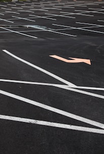 An empty parking lot with neatly painted white lines indicating parking spaces. An orange arrow on the asphalt points in a direction, offering guidance for traffic flow. The surface is smooth with no visible vehicles or people present.