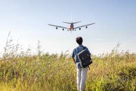 a man with a backpack looking at an airplane in the sky