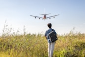 a man with a backpack looking at an airplane in the sky