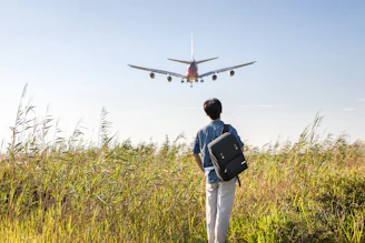 a man with a backpack looking at an airplane in the sky