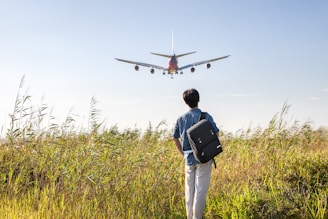 a man with a backpack looking at an airplane in the sky