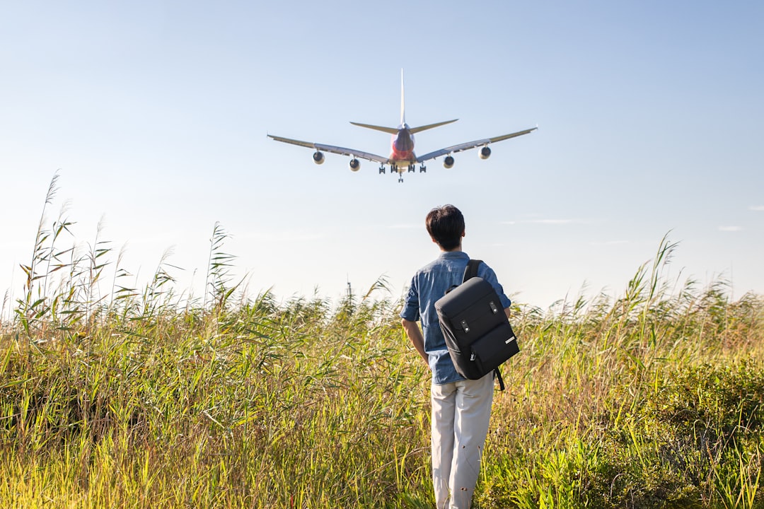 a man with a backpack looking at an airplane in the sky,