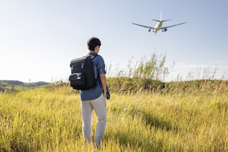 a man with a backpack looking at an airplane in the sky