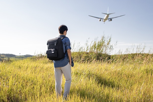 a man with a backpack looking at an airplane in the sky