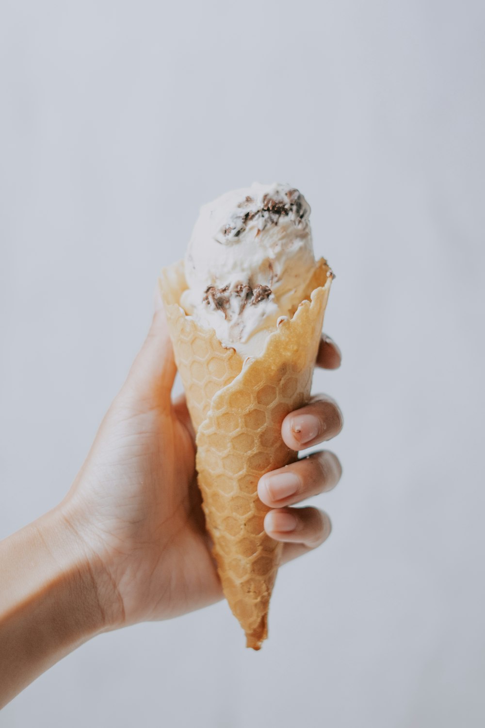 a hand holding an ice cream cone filled with whipped cream