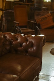 A cozy room with vintage furniture, including a tufted leather couch and an old wooden wheelchair. The lighting is warm and natural, creating a nostalgic atmosphere.