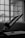 A drafting table with a propped-up drawing board is in the foreground, positioned next to a large window with grid-like panes. Natural light streams in through the window, casting soft shadows on the table and emphasizing the indoor setting.