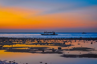 A serene beach at sunset with crystal-clear water and traditional fishing boats.