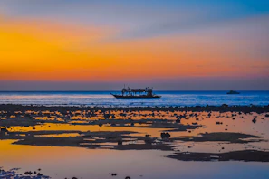 Sunset over a serene beach with traditional dhow boats in Zanzibar.