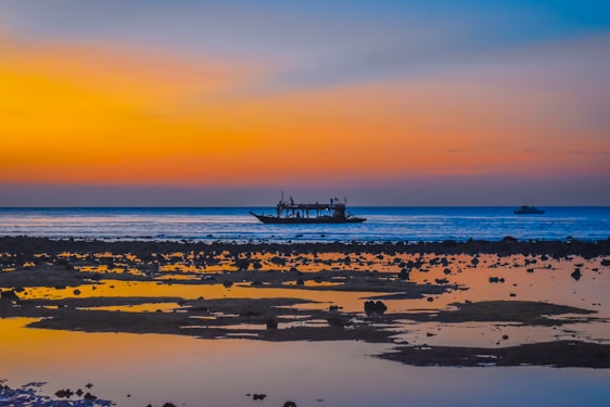 A serene Thai beach at sunset with a traditional longtail boat resting on the shore.