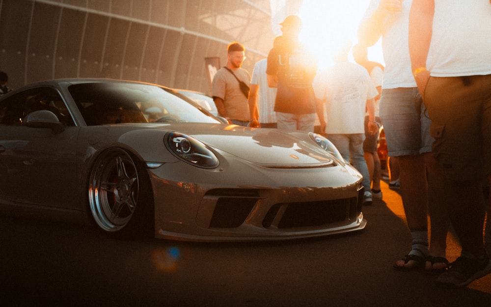 a group of people standing around a silver sports car