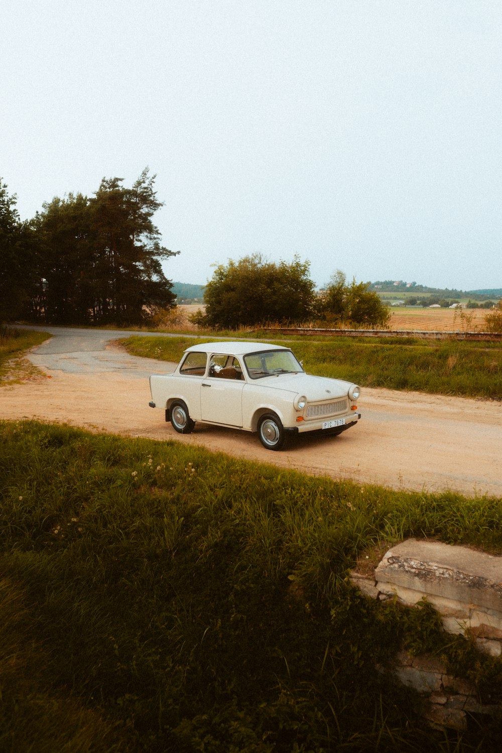 a small white car parked on a dirt road