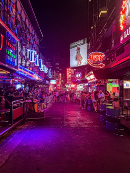 A vibrant street scene in Manila at night, with neon yellow signs glowing against a dark sky.