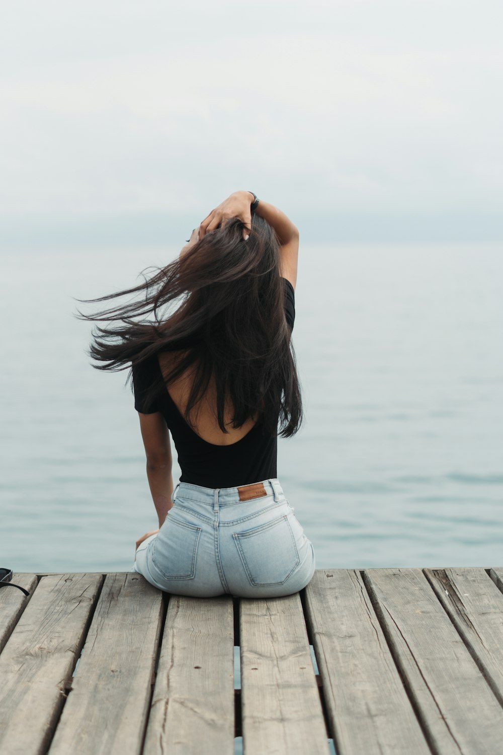 a woman sitting on a dock with her hair blowing in the wind