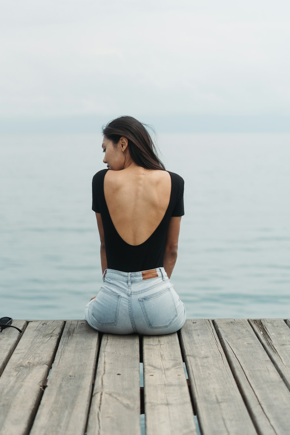 eine frau, die auf einem dock sitzt und auf das wasser schaut