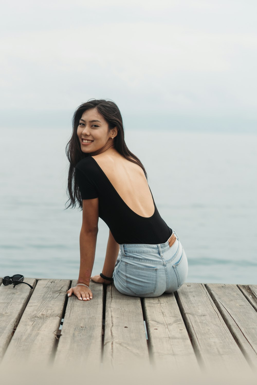 a woman sitting on a wooden dock next to the ocean