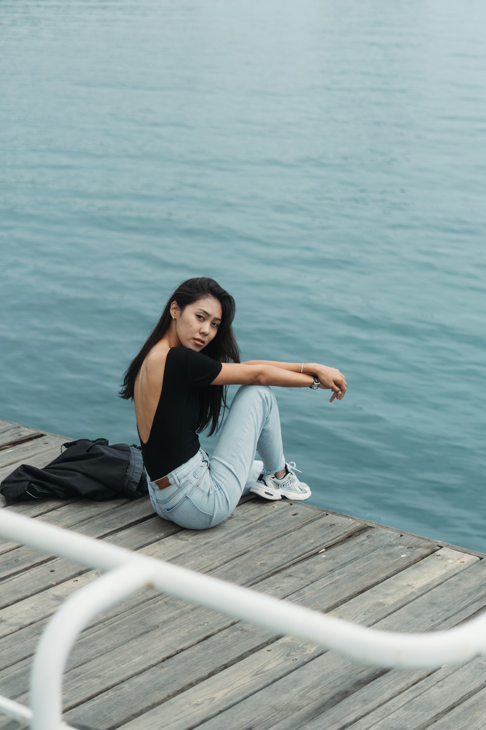 a woman sitting on a dock next to a body of water