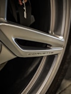 Close-up view of a metallic wheel with the word 'Corvette' embossed on it. The wheel features sleek design elements and grooves.