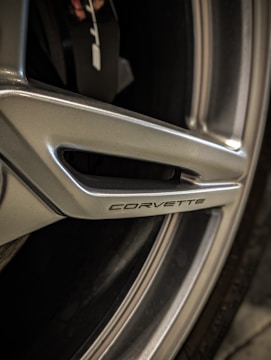Close-up view of a metallic wheel with the word 'Corvette' embossed on it. The wheel features sleek design elements and grooves.