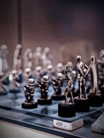 A collection of small, metallic figurines displayed on a reflective surface. These figurines resemble characters from the Star Wars universe, intricately crafted and placed on black pedestals. The background is softly blurred, emphasizing the shiny and detailed figures in the foreground.