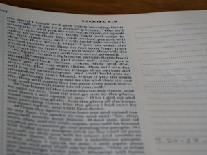 A close-up view of a page from a Bible open to the book of Ezekiel, with text visible and partially focused on verses discussing divine warnings and moral guidance. The page appears to be on a desk, and part of the page is slightly out of focus.