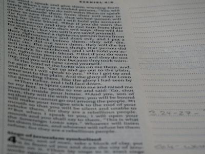 A close-up view of a page from the Bible with text focusing on a specific passage. The right side of the image features a notebook with lined pages for note-taking.