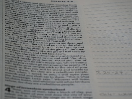 A close-up view of a page from the Bible with text focusing on a specific passage. The right side of the image features a notebook with lined pages for note-taking.