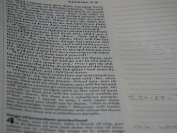 A close-up view of a page from the Bible with text focusing on a specific passage. The right side of the image features a notebook with lined pages for note-taking.