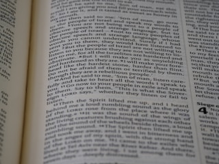A close-up view of a page from a book, featuring text printed in a column layout. The text appears to be from a religious or philosophical work, with words and phrases presented in a structured format. The focus is on the middle of the page, with other text slightly blurred in the foreground and background.
