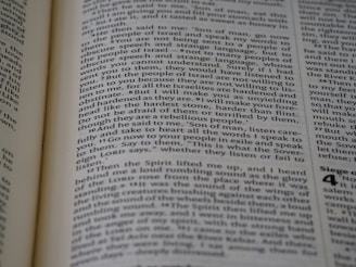 A close-up view of a page from a book, featuring text printed in a column layout. The text appears to be from a religious or philosophical work, with words and phrases presented in a structured format. The focus is on the middle of the page, with other text slightly blurred in the foreground and background.