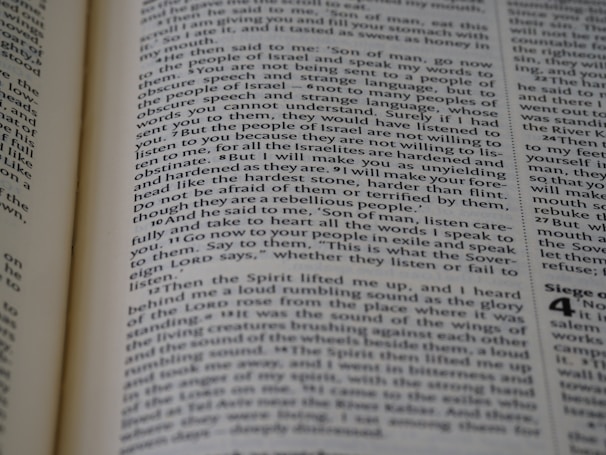 A close-up view of a page from a book, featuring text printed in a column layout. The text appears to be from a religious or philosophical work, with words and phrases presented in a structured format. The focus is on the middle of the page, with other text slightly blurred in the foreground and background.